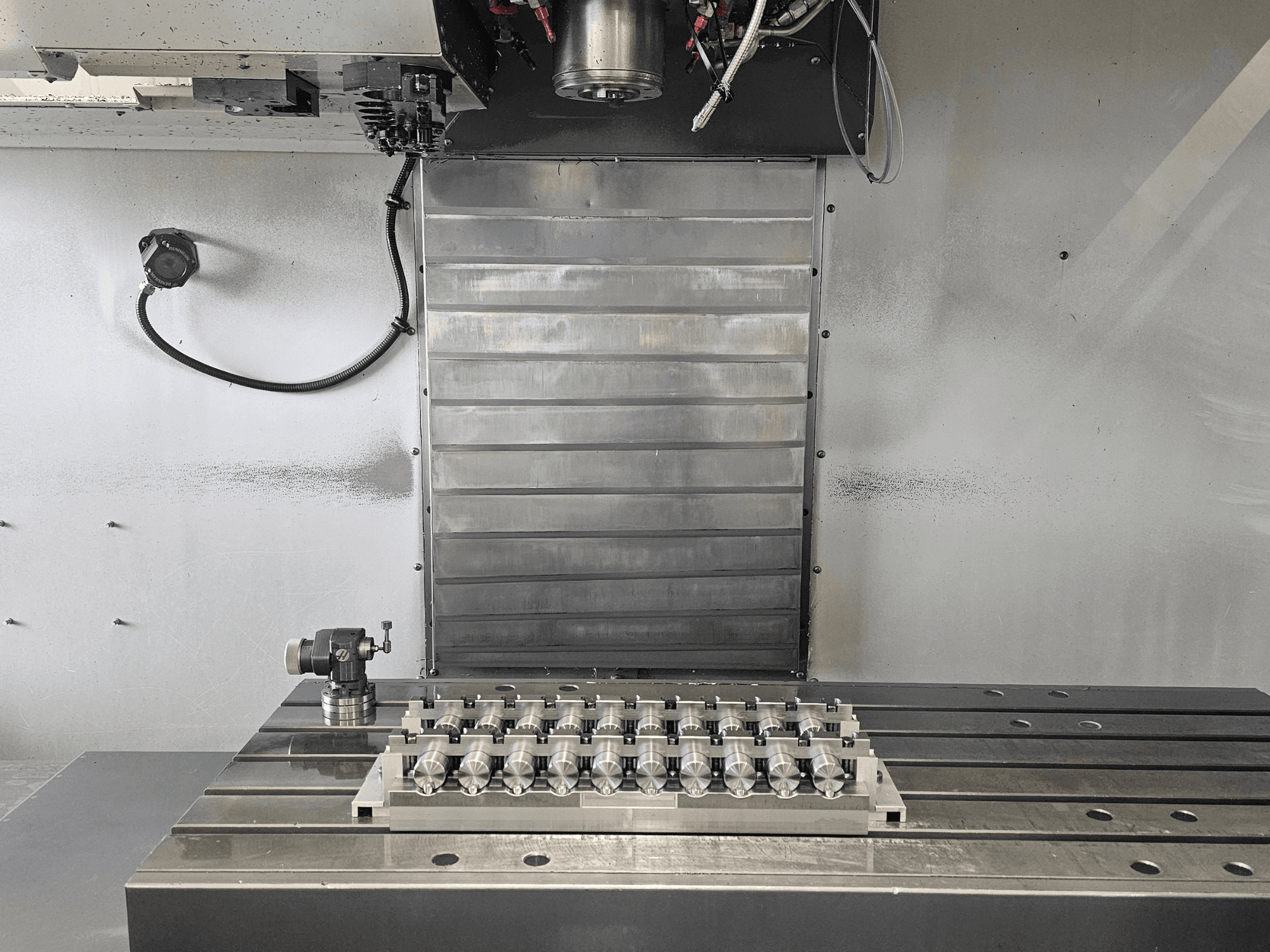 Metal tabla ve kontrol mekanizmaları üzerinde hassas işlenmiş bir parça içeren bir CNC freze makinesinin çalışma alanının önden görünümü.