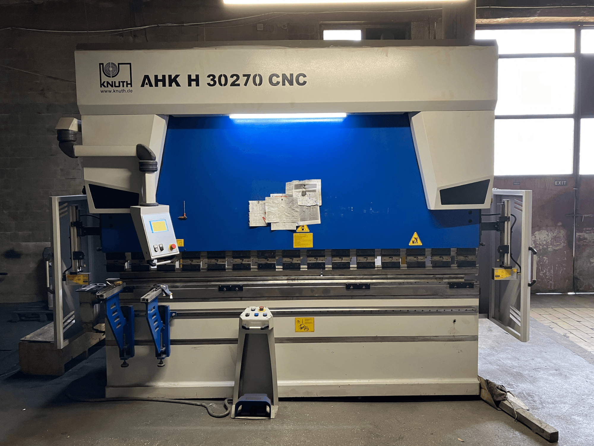 Bir atölyede bulunan KNUTH AHK H 30270 CNC kant press makinesi, önden görünüm; kontrol paneli ve mavi/beyaz tasarımı gösterilmekte olup, yan kapısı açık durumdadır.