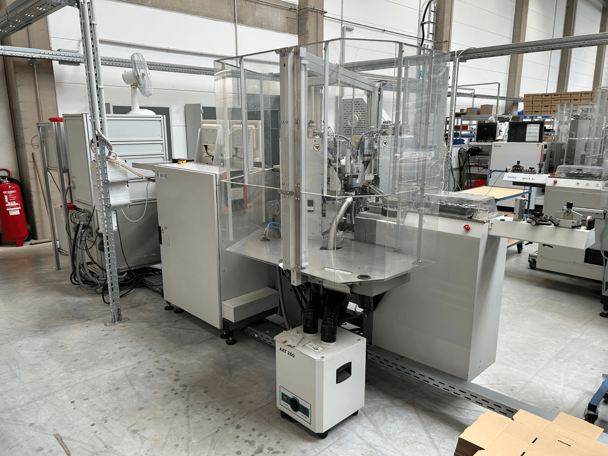 Bir fabrika ortamında kullanılan KOMAX Alpha 433 L otomasyon ekipmanı. Şeffaf güvenlik muhafazası ve çeşitli kontrol panelleri ile donatılmıştır.