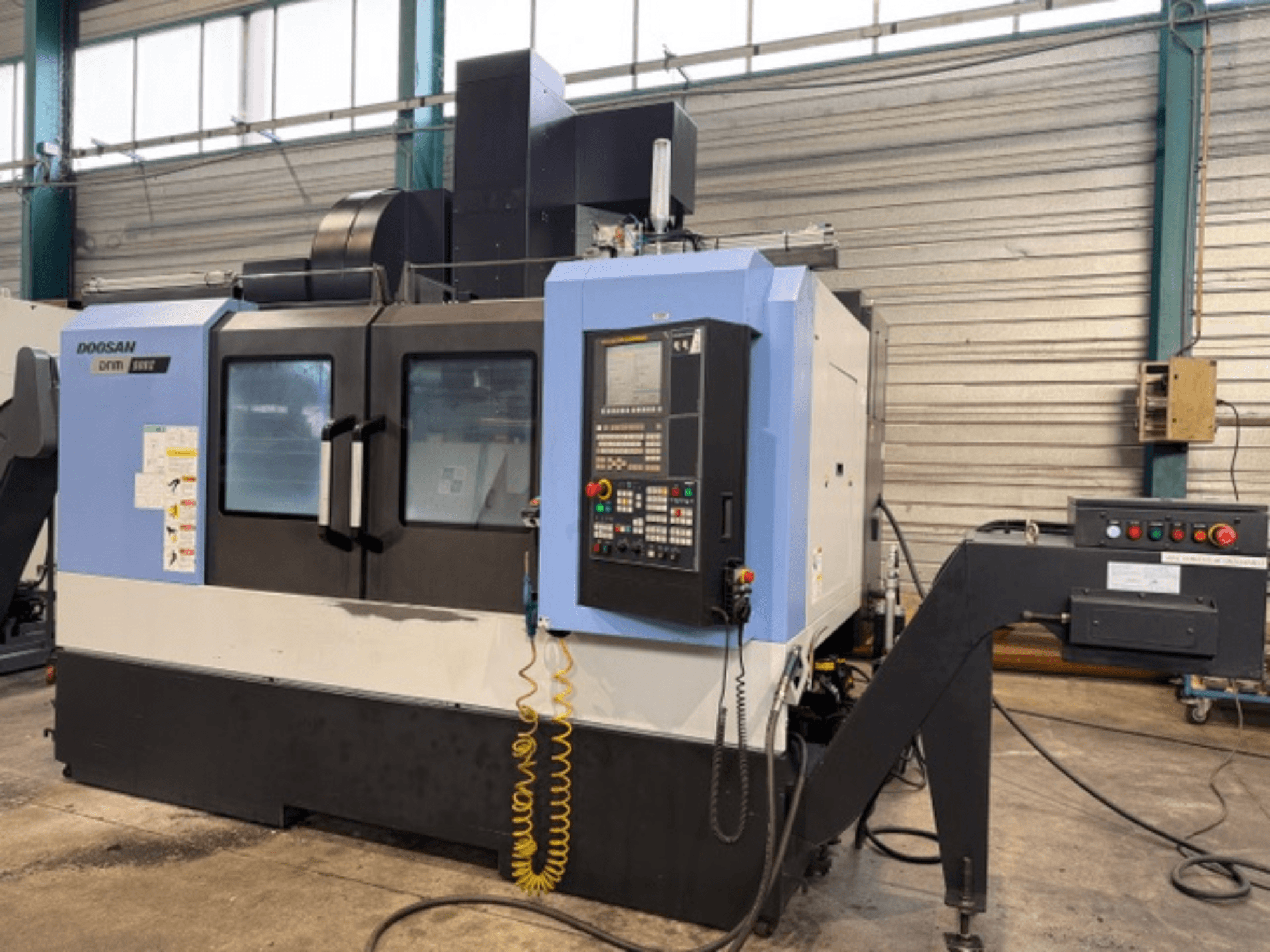 Doosan DNM 500II CNC freze makinesinin önden görünümü, kontrol paneli ve takım tutucusu, fabrika ortamında.
