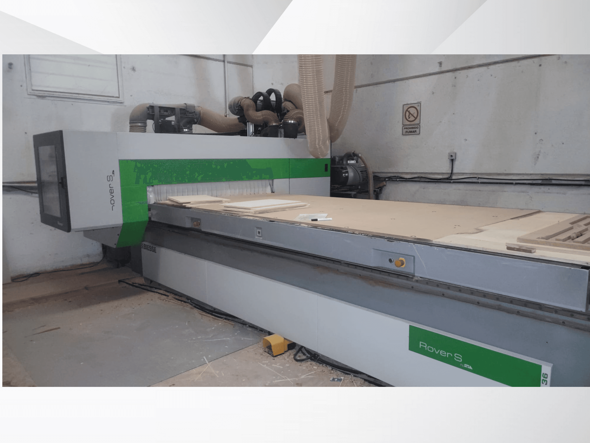 Ahşap paneller ve toz emme hortumları ile geniş bir çalışma yüzeyine sahip Biesse Rover S CNC makinesinin önden görünümü.
