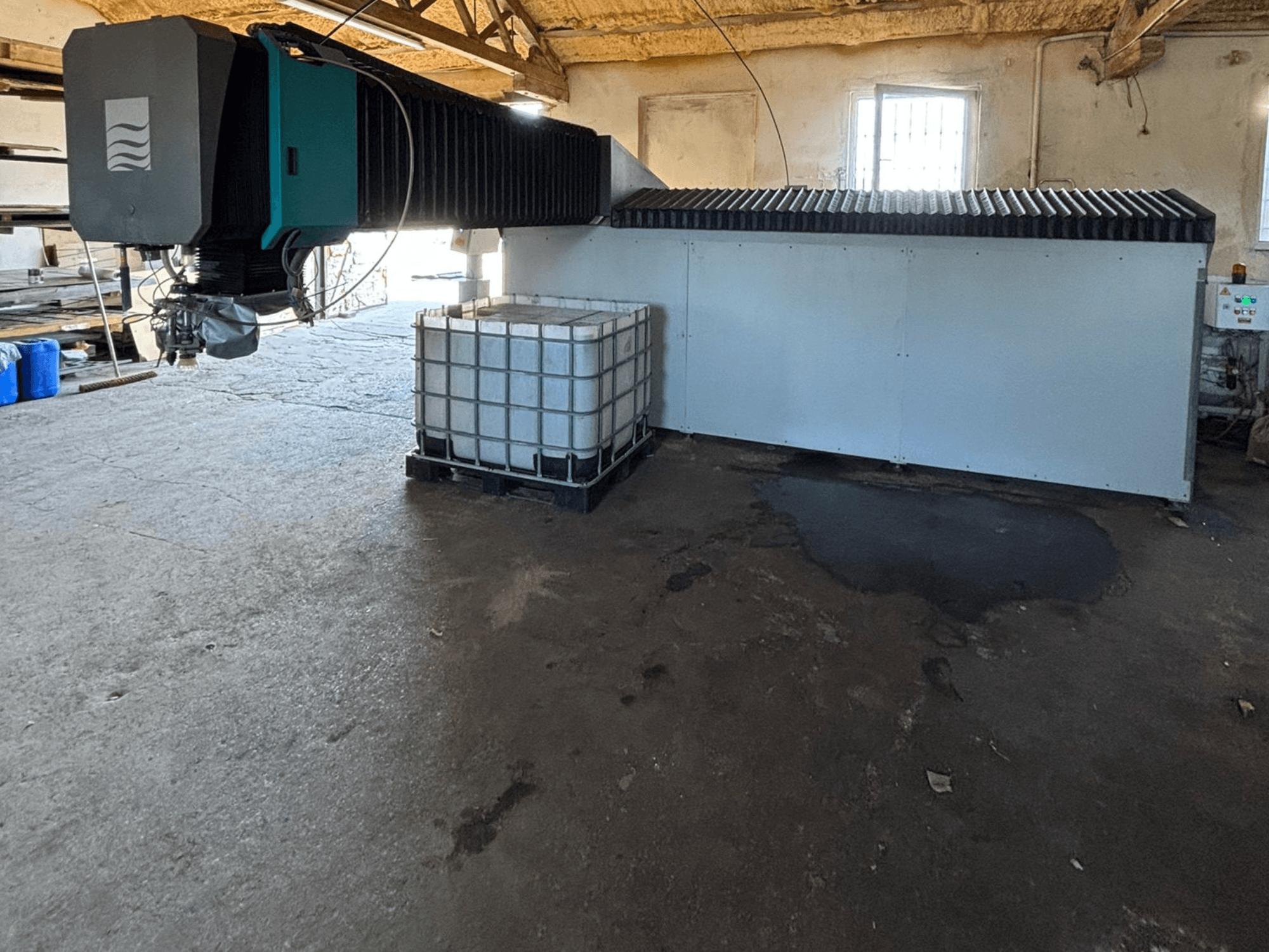 Bir atölyedeki endüstriyel su jeti makinesi, yandan görünüm, yanında büyük bir su deposu ve kontrol paneli görünüyor.