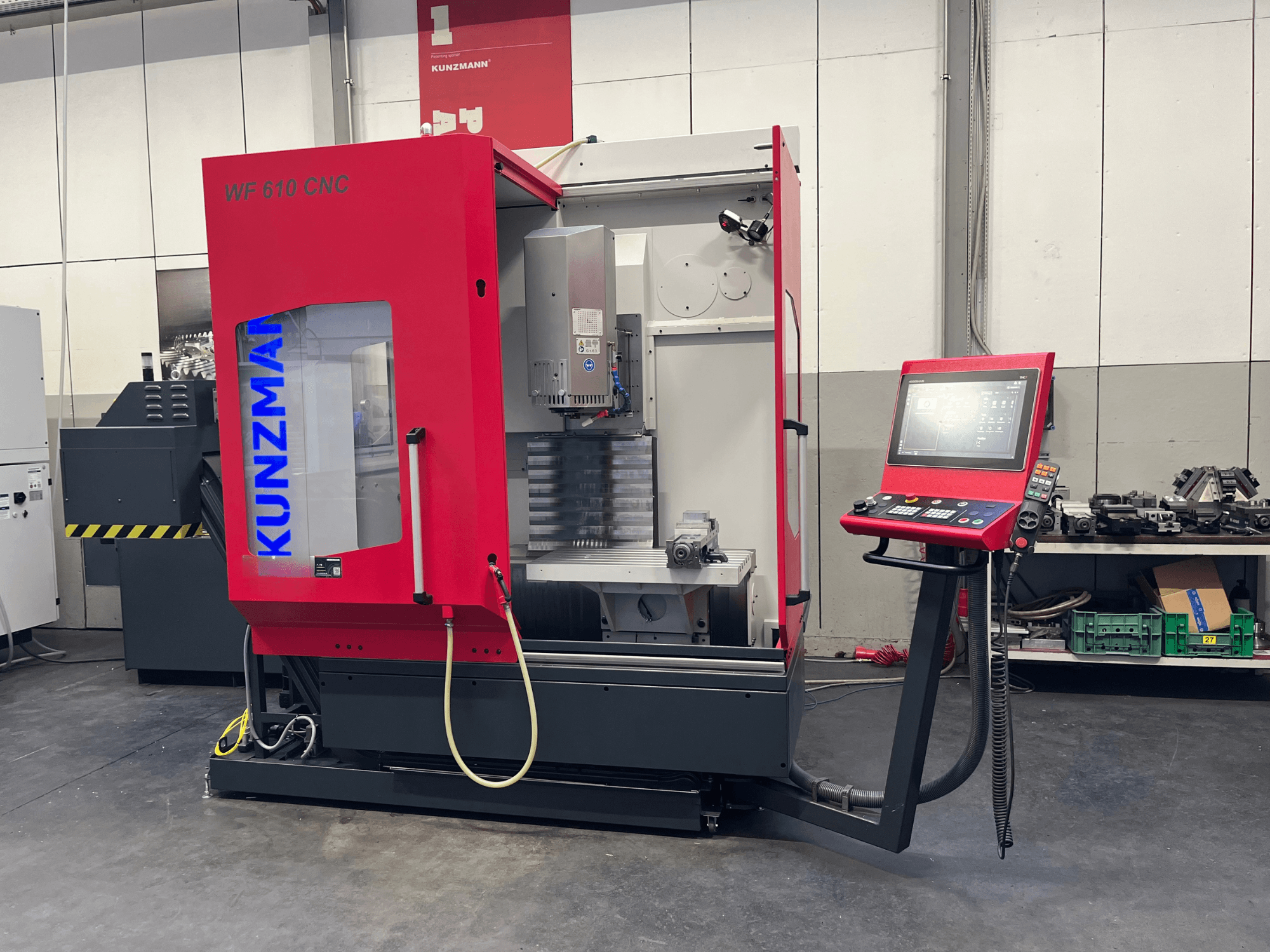 Bir atölyede bulunan, kontrol paneli ve görünür makine bileşenleri ile donatılmış KUNZMANN WF 610 CNC dikey işleme merkezi.