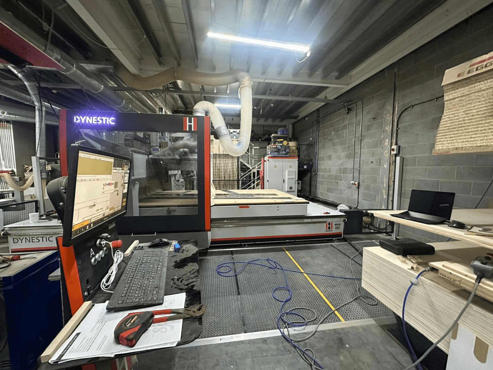 HOLZHER Dynestic 7535 ahşap değirmeni atölyede, kontrol paneli, monitör ve çalışma masasındaki malzemeler, önden görünüm.