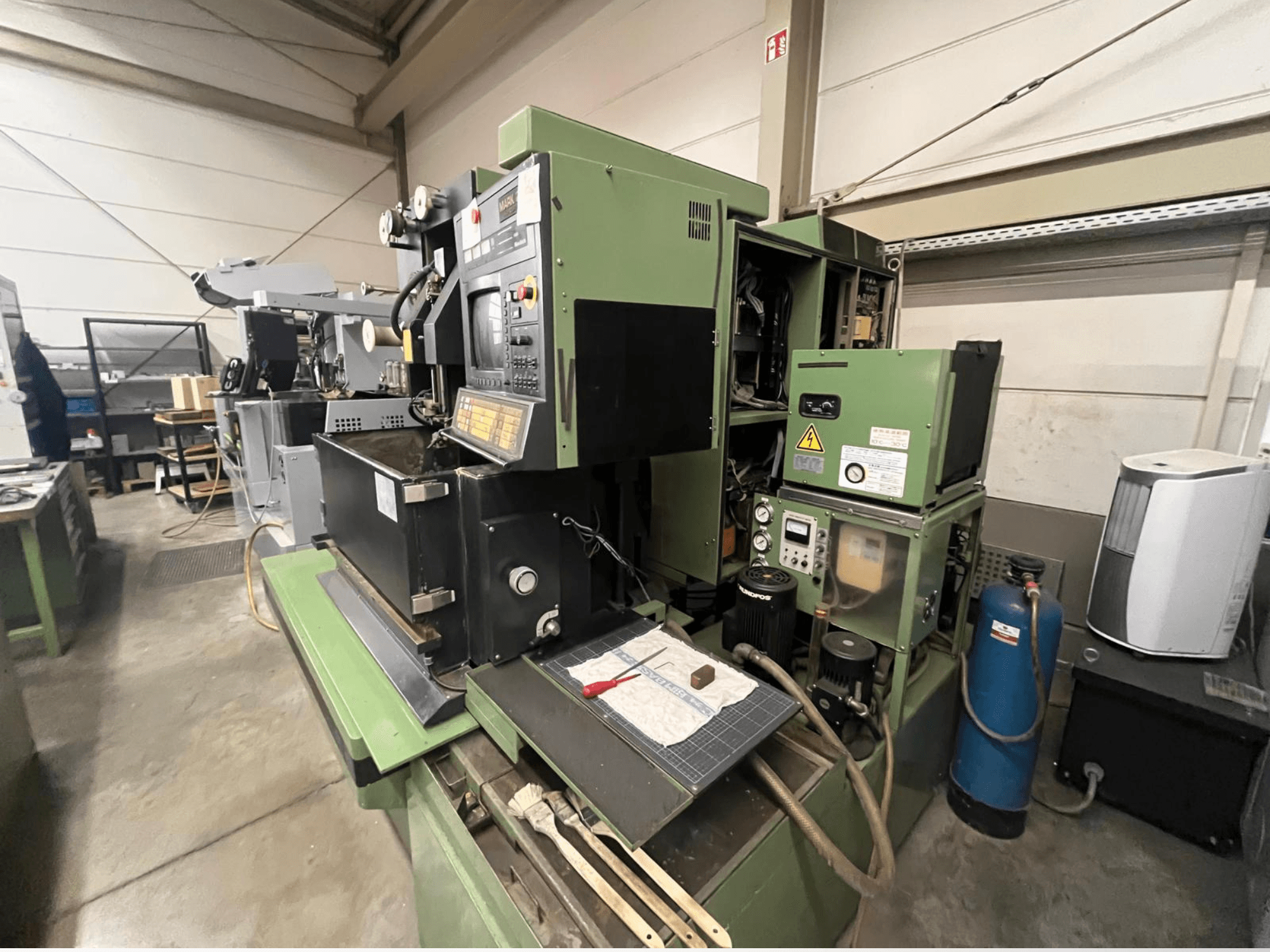 Kontrol panelli yeşil endüstriyel makine, yandan görünüm; hidrolik bileşenler ve aletli çalışma alanı yüzeyi içerir.