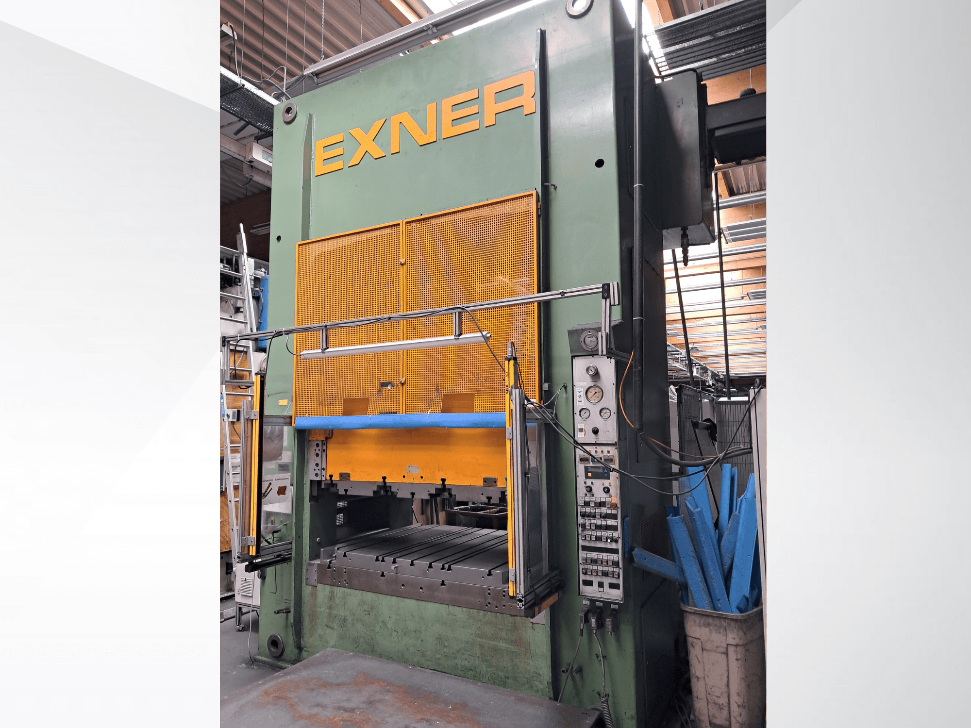 EXNER EX SBR 150 hidrolik pres, önden görünüm; kontrol paneli, mavi güvenlik çubuğu ve tel örgü koruyucu ile donatılmış, bir atölye ortamında yer almaktadır.
