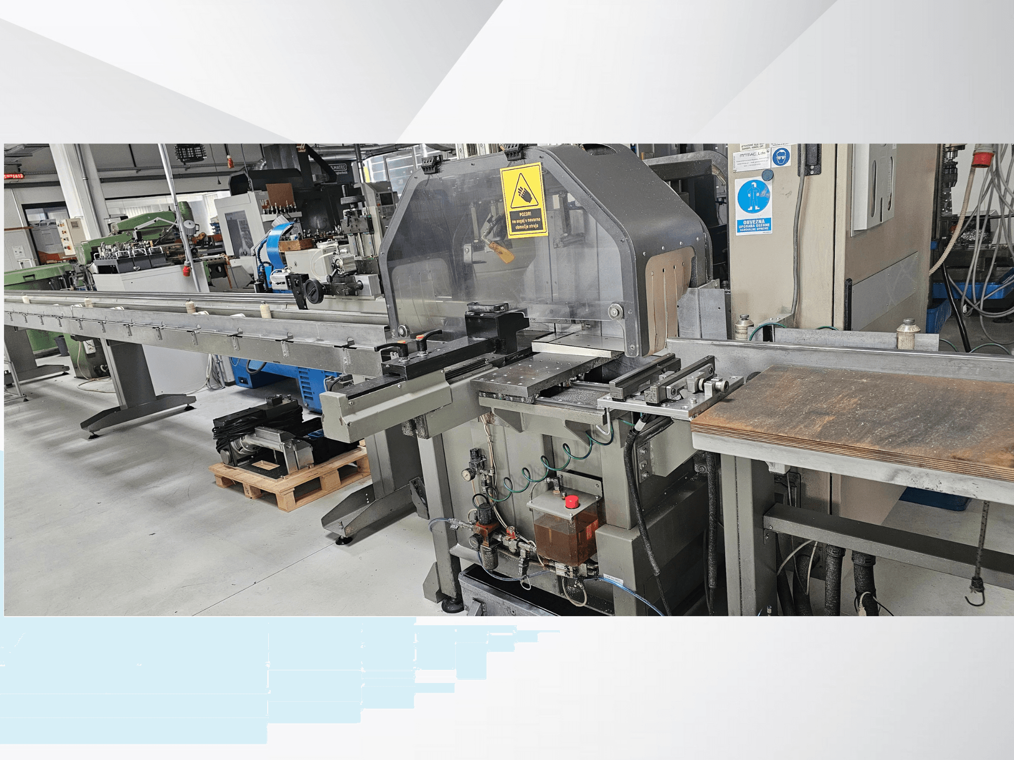 Uzun bir konveyör, kontrol paneli ve güvenlik uyarıları içeren yandan görünümlü endüstriyel kesim makinesi.