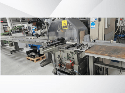 Uzun bir konveyör, kontrol paneli ve güvenlik uyarıları içeren yandan görünümlü endüstriyel kesim makinesi.
