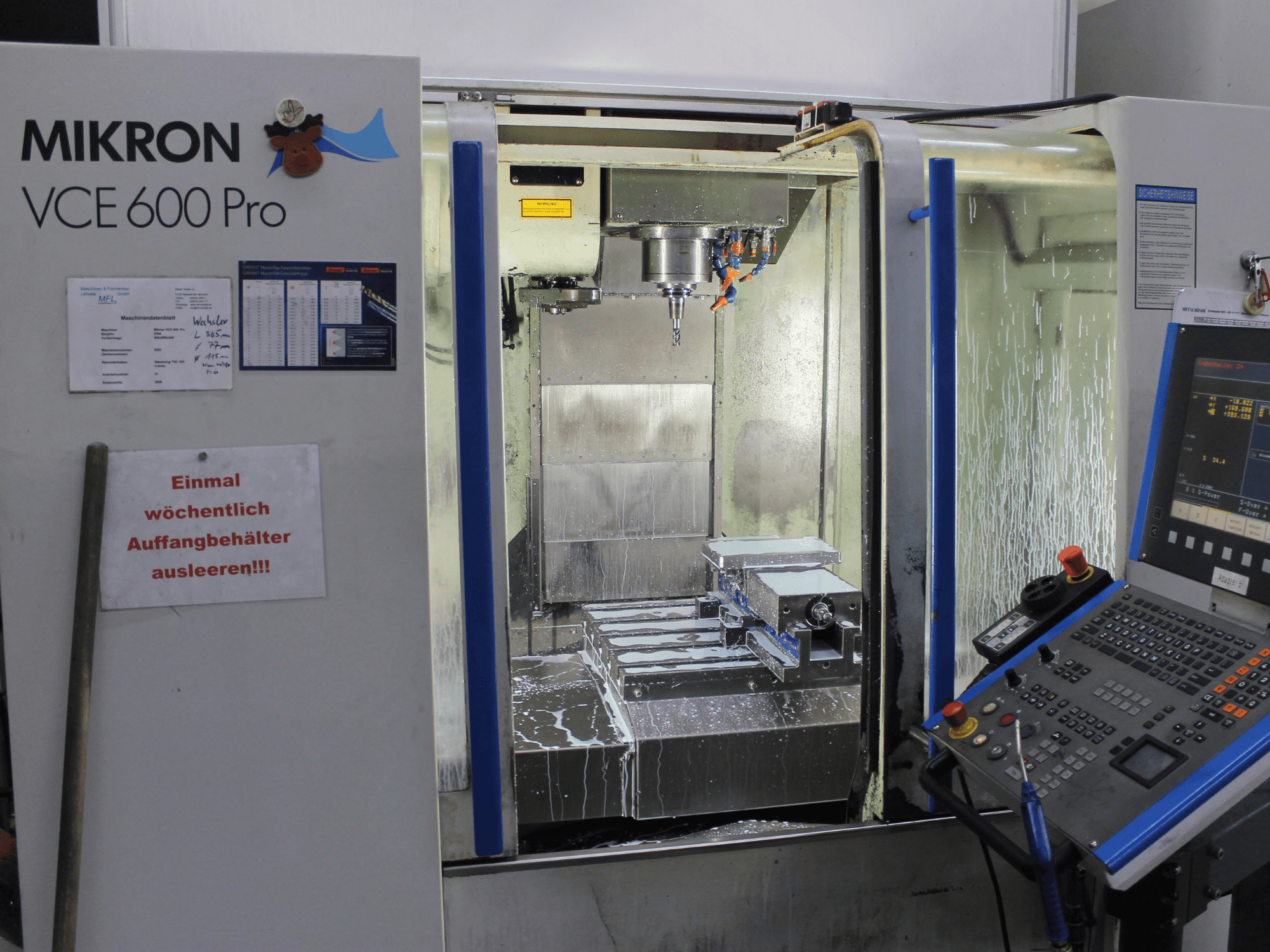 Mikron VCE 600 Pro işleme merkezi, önden görünüm, kesme takımları, soğutma sıvısı spreyi ve düğmeli kontrol paneline sahiptir.