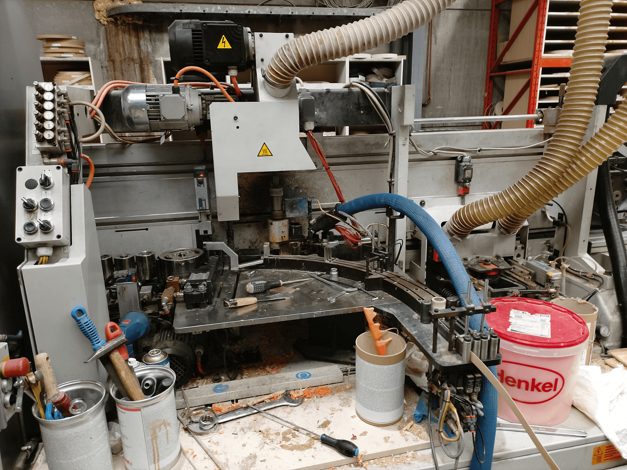 BIESSE Edge Stram B1 kenar bantlama makinesi önden görünümde, ahşap talaşları arasında makineler, hortumlar ve çalışma aletleri sergileniyor.