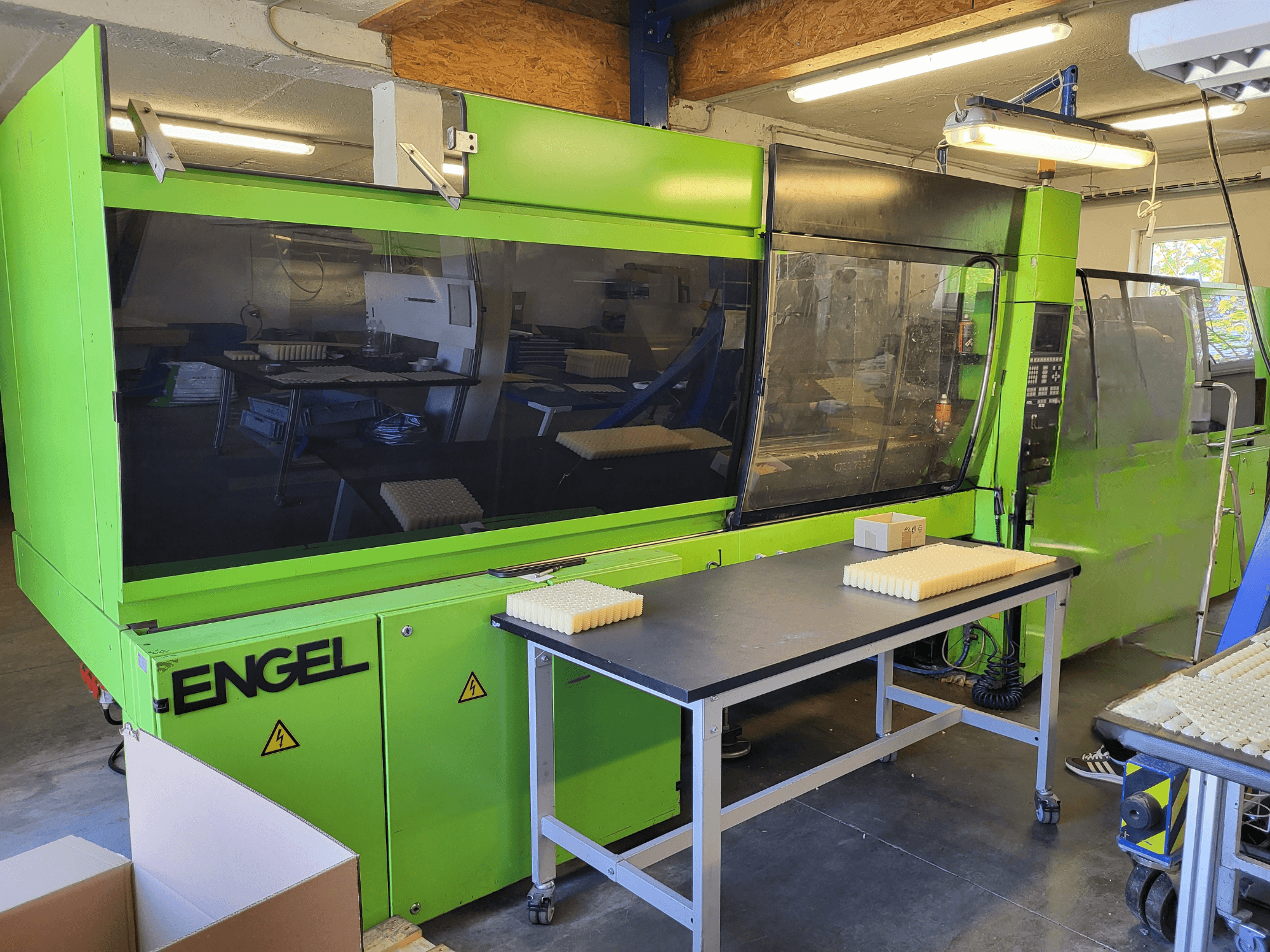 Green Engel ES1800/300HL hidrolik enjeksiyon kalıplama makinesinin önden görünümü; çalışma masası üzerinde istiflenmiş malzemeler.