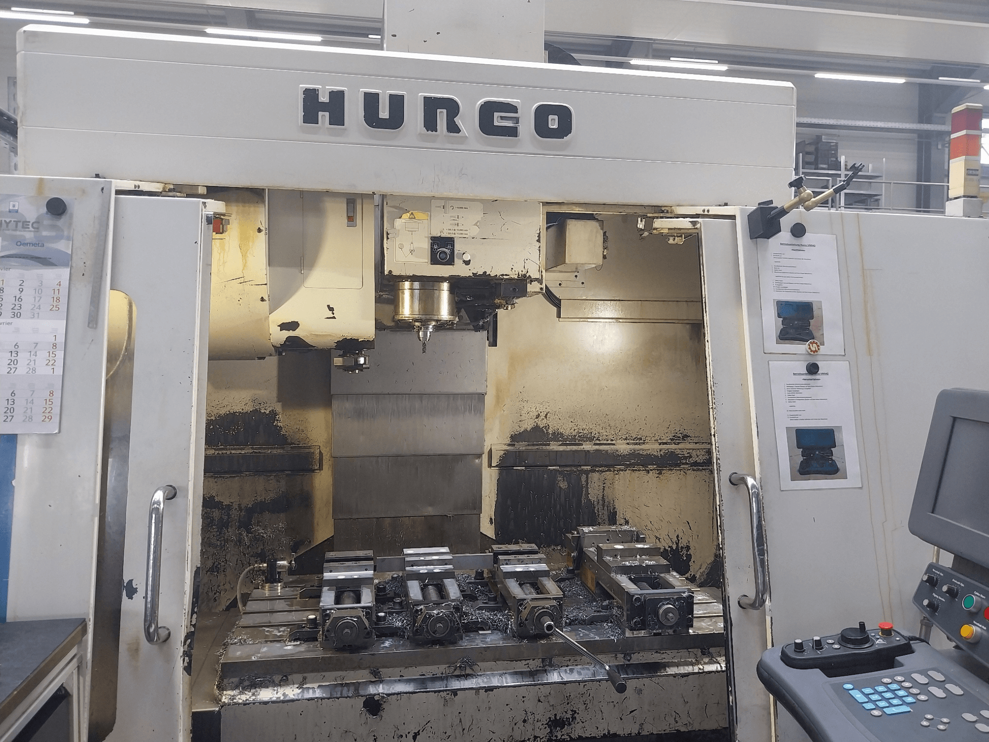 Hurco VMX 42 dikey işleme merkezi önden görünüm, fikstürler ve kontrol paneli ile çalışma masasını gösteriyor, hafif aşınmış durumda.