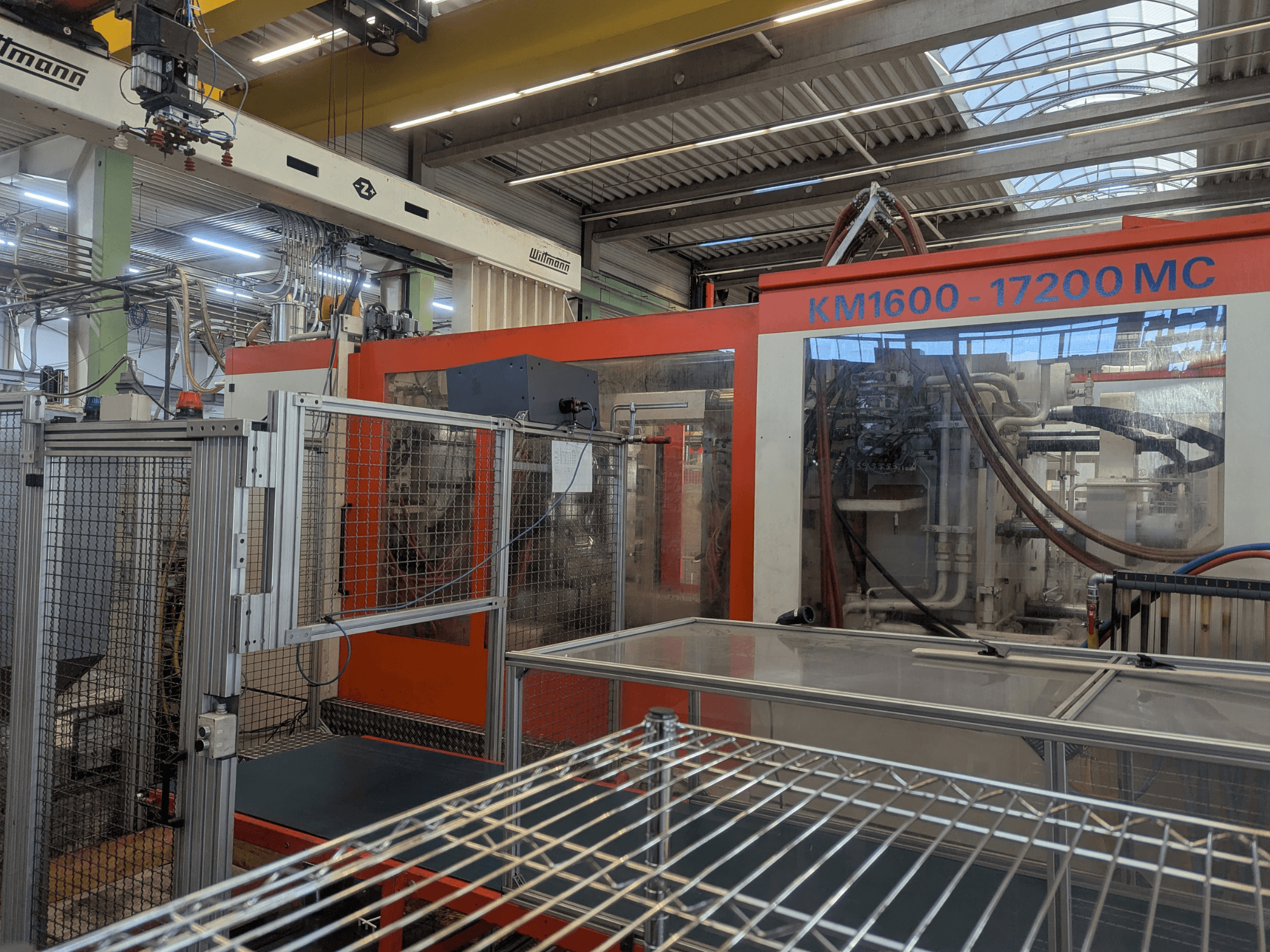 Hidrolik enjeksiyon kalıplama makinesi Krauss Maffei KM 1600-17200MC, görünür kontrol paneli ve hidrolik hatları ile önden görünüm.