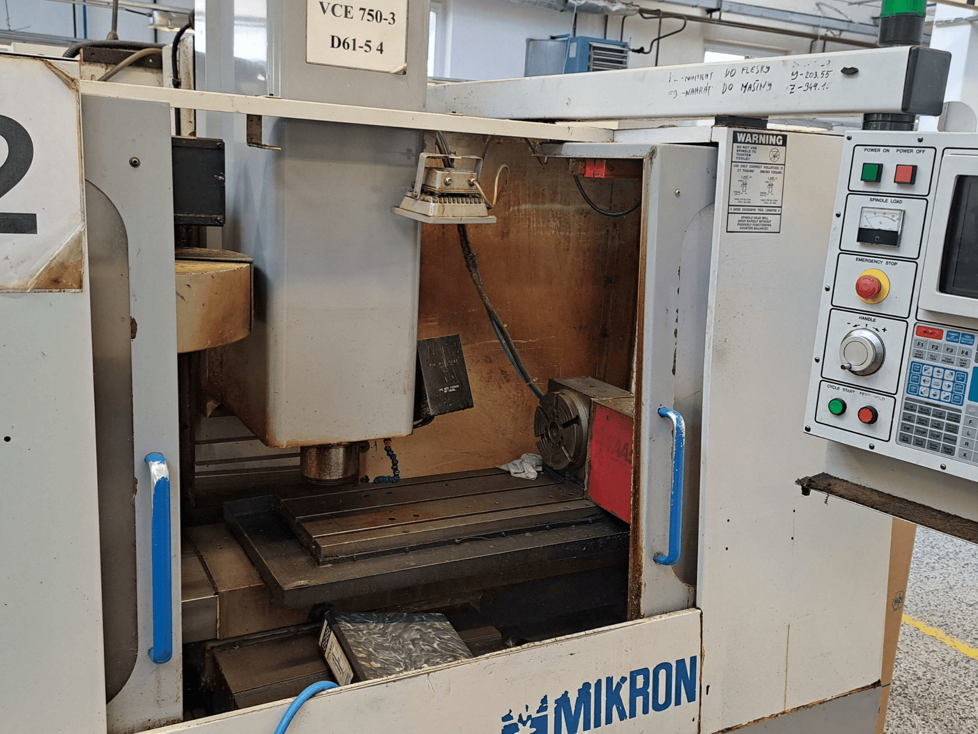 Mikron VCE 750-3 freze makinesinin önden görünümü, iş milini, kontrol panelini ve çalışma tablasını teknik detaylarla birlikte gösterir.