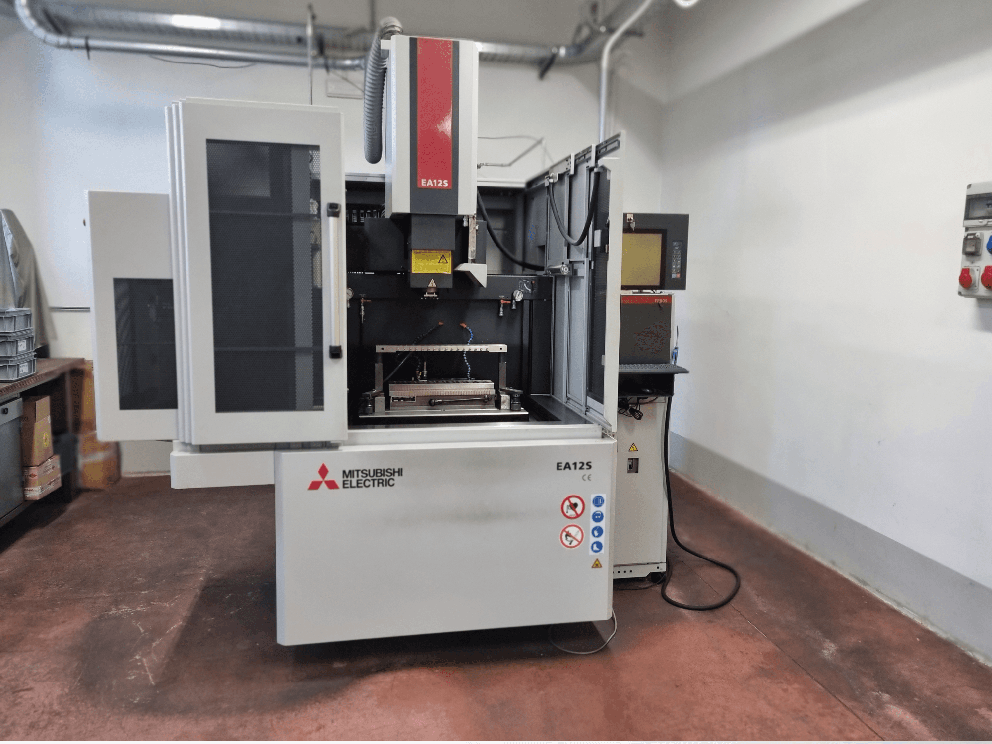 Mitsubishi Electric EA12S tel kesme makinesi, önden görünüm, açık kapılar, kontrol paneli ve güvenlik etiketleri.