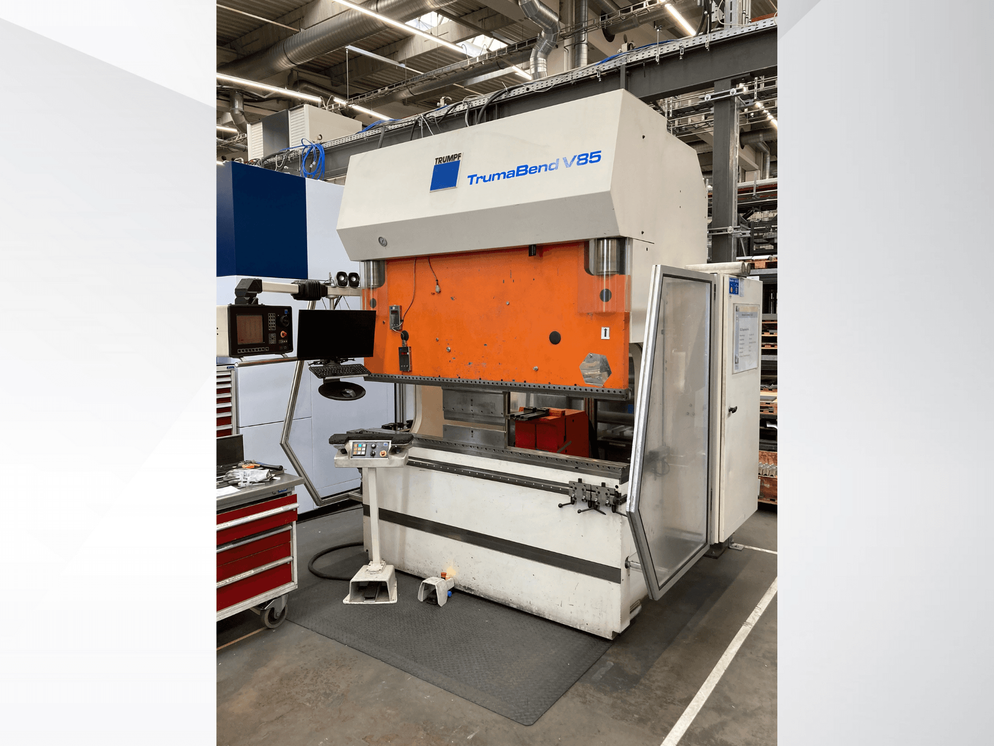Fabrikadaki TruMatic V85 bükme makinası, turuncu ön panel, kontrol ekranı ve açık yan kapı, yandan görünüm.
