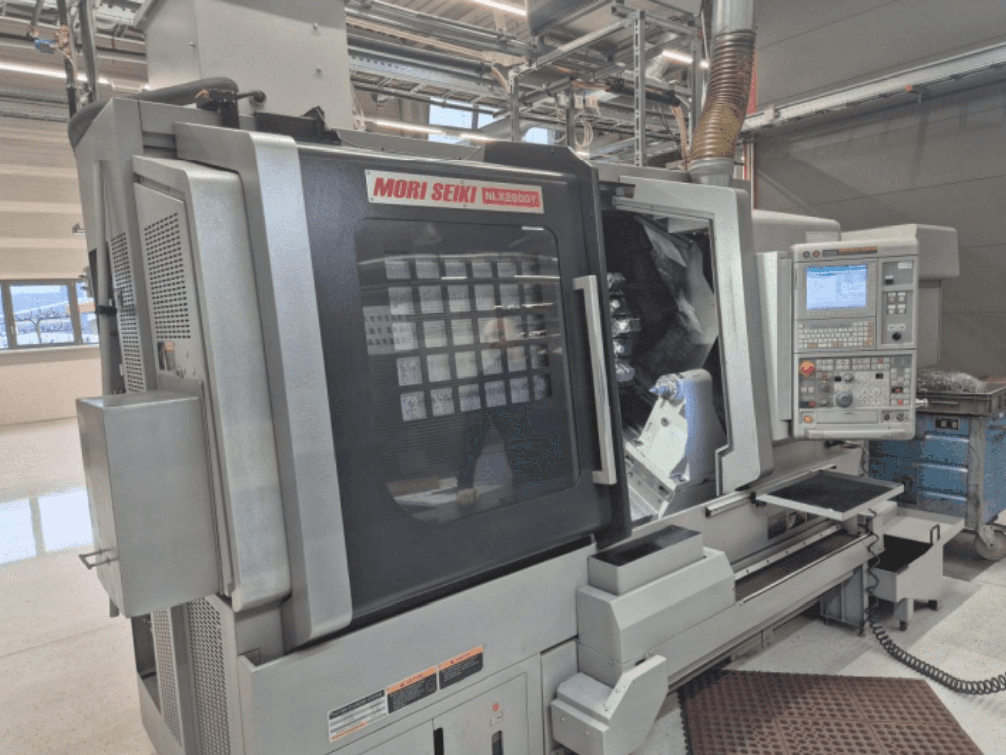 MORI SEIKI NL2500Y CNC torna makinesi fabrika ortamında, kontrol paneli ve iş parçası haznesini gösteren önden görünüm.