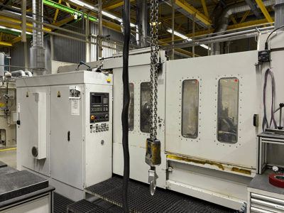 Kontrol panelli endüstriyel CNC makinesi, yandan görünüm; fabrika ortamında pencereler, zincirler ve metal bileşenler bulunur.