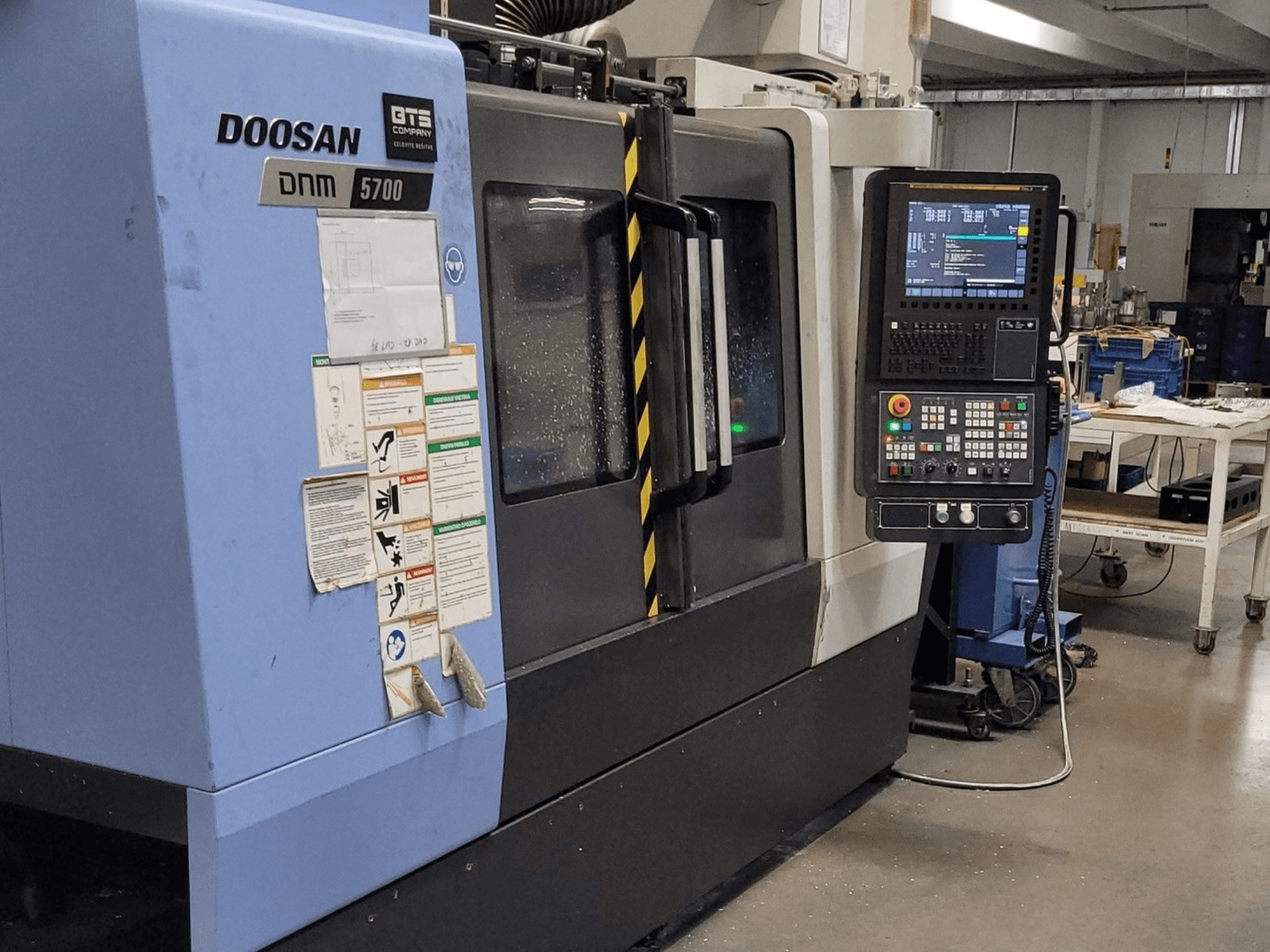 DOOSAN DNM 5700 dikey işleme merkezi, önden görünüm; kontrol paneli ve çalıştırma düğmeleri gösterilmektedir.